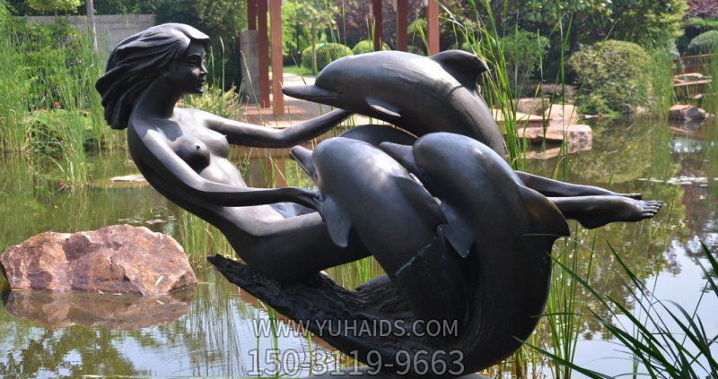 河边一位美女与多只石雕海豚玩耍的海豚雕塑